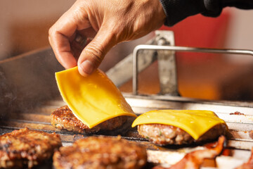 Man adding cheese on the top of a burger in a grill