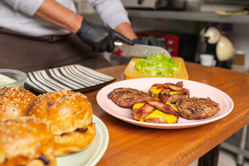 Chef cutting lettuce next to a dish with grilled burgers