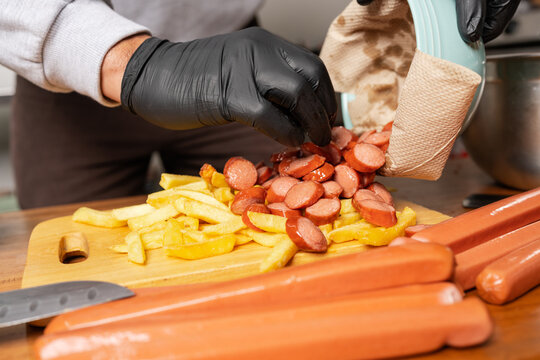 Man mixing frankfurts with fries in a kitchen