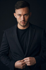 Modelling snapshots. Narcissistic self-confident tanned attractive handsome man in classic suit jacket looks at camera posing isolated in over black studio background. Fashion offer. Copy space for ad