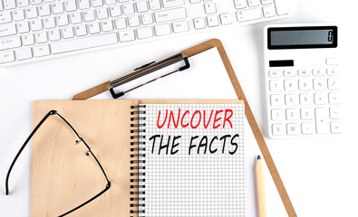 Notebook with the word UNCOVER THE FACTS with keyboard and calculator on the white background