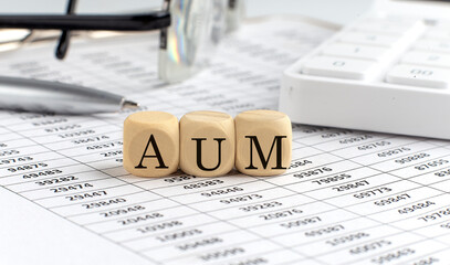 wooden cubes with the word AUM -ASSET UNDER MANAGEMENT on a financial background with chart,...