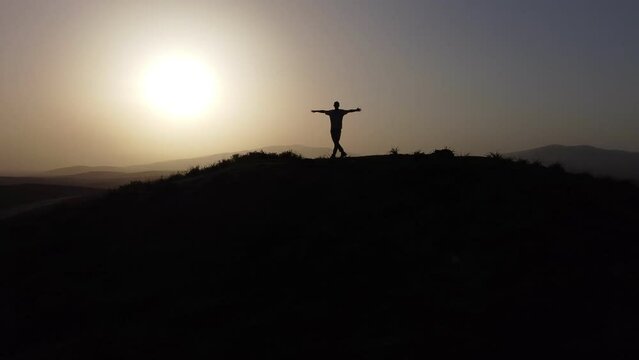 Silhouette of a man with arms raised on a hill and sunset.