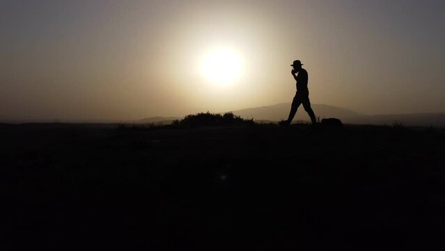Silhouette of a man with fedora hat on sunset on tumulus hill.