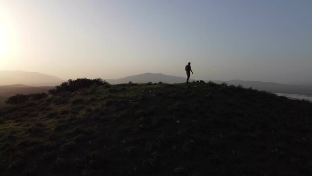 Silhouette of a man with fedora hat on sunset on tumulus hill.