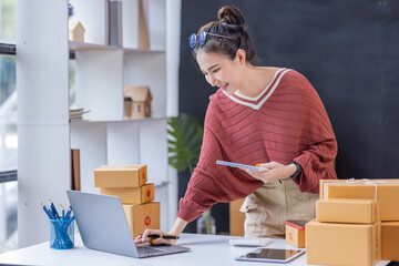 SME Online seller Young Asian woman freelance working on laptop tablet and box, checking online...