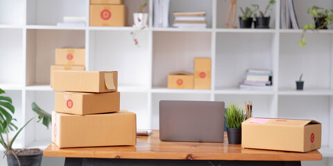Parcel boxes on shelf and color shopping bags placing near laptop on table. SME business on shopping online at home office packaging on background is popular business.