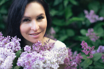Naklejka premium Portrait of an attractive woman surrounded by lilac bushes. Spring and summer, seasonal photos. Front view.