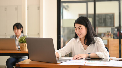 Fototapeta na wymiar Asian female accountant using laptop and working with financial reports at her office desk