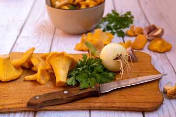 fresh chanterelle mushrooms with fresh vegetables, onions, garlic, parsley, on a board with a cooking knife, top view.