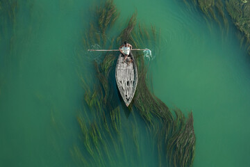 Fishermen are seen floating on top of algae as they search for potential catch in the sharp green...