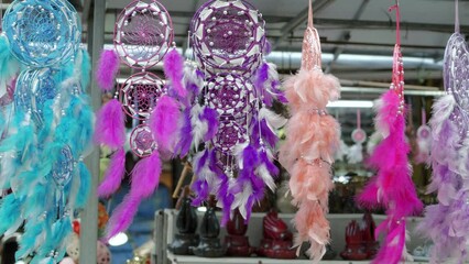 A stationary footage of a breezy afternoon with hanging dream catchers with thick feathers, various colors and sizes that are hung for selling. Colors: aqua blue, purple, violet, flesh, pink, lavender - Powered by Adobe