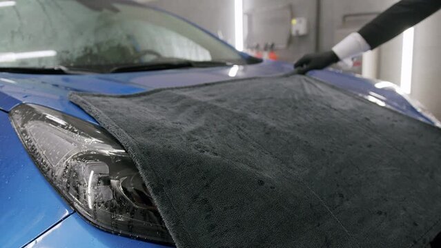 Close up of elegant man drying a brand new blue car with a special blanket in garage 