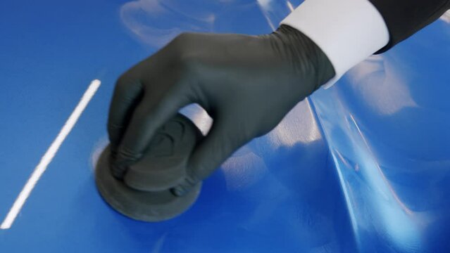 Close-up of a man in suit and gloves waxing the hood of a new car with a sponge.
