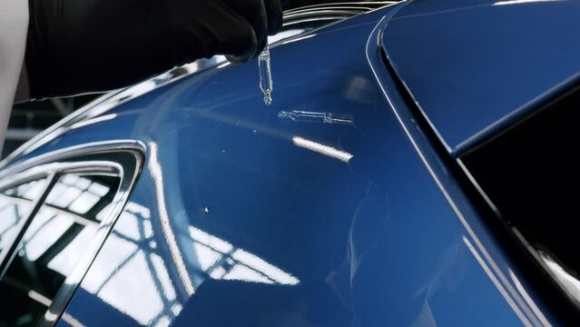 Carefully checking hydrophobicity effect on new car using pipette and water in slow motion. Low angle view.