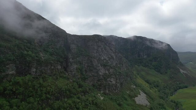 A magnificent drone shot through a valley in Northern Scotland. The shot pans over treetops up to cloudy mountain peaks and up to a mountaintop lake.