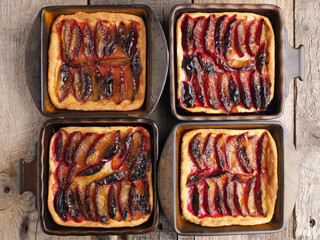 Freshly baked plum cake in ceramic bowls on a rustic kitchen table, top view