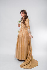 Fototapeta premium Full length portrait of a woman in a gold dress in the style of the rococo era, standing and posing with a flower in hand isolated on a white background.
