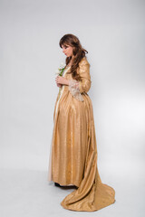 Full length portrait of a woman in a gold dress in the style of the rococo era, standing and posing with a flower in hand isolated on a white background.