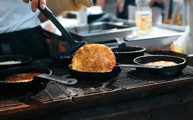Close-up of chef cooking potato pancakes at street food festival. Pan fried draniki, hash brown