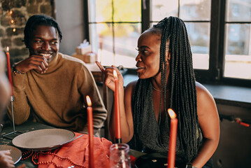 Best friends celebrating new year. Young people with candles, sitting at dining table. Diverse students during christmas party at home, smiling and laughing.