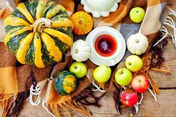 The concept of autumn nature. Lying vegetables on the background of a wooden texture. Yellow and orange pumpkin, red and green apples, tea and autumn maple leaves. Thanksgiving Day Background