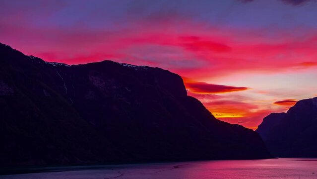 A stunning pink sunset reflects of the water in the fjord below the rugged mountains - time lapse