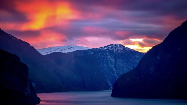 Brilliant sunset pink and purple clouds cross the sky above steep mountainsides plummeting into a misty fjord in Scandinavia - time lapse 