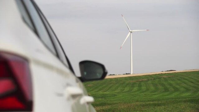 Side of white car and windmill on meadow in background, automobile industry change concept