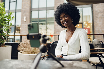 Portrait of smiling woman with afro hairstyle on video call sitting in cafe