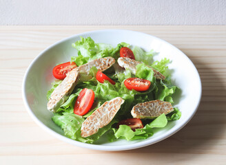tempeh or tempe salad with tomato and green vegetable in white plate on wooden table.