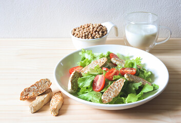  tempeh in salad dish, soy bean seeds in white bowl, and soy milk on wooden table, products of soy beans.