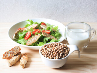 soy bean seeds in white bowl, tempeh in salad dish and soy milk on wooden table, products of soy beans.