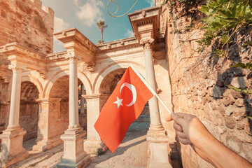 Turkish Flag in hand and famous gate or Hadrian arch in Antalya. Travel landmarks and must-visit tourist and sightseeing sites in Turkey