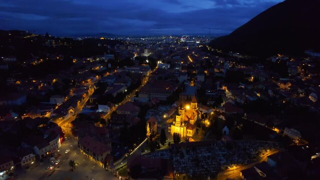 Aerial drone view of the Saint Nicholas Church in Brasov at night, Romania. Medieval church with multiple buildings and roads with nightlights