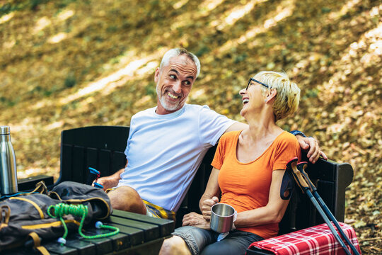 Mature couple sitting and drink coffee while resting in the forest after hiking.
