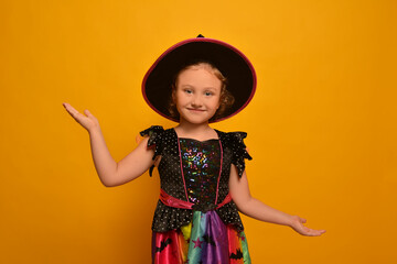 Halloween child in witch costume looking at camera, smiling and demonstrating copy space advert on...