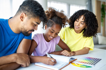 Front view of African American parents helping their daughter with homework at table, Photo of a young girl being homeschooled by her parents