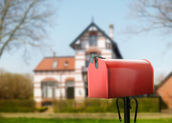 Red letter box and blurred view of modern house with beautiful garden on sunny day, space for text