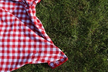 Checkered picnic tablecloth on fresh green grass, top view. Space for text