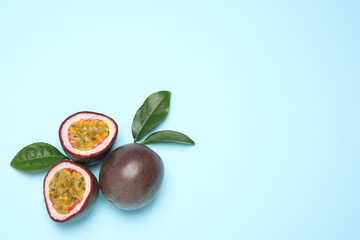 Fresh ripe passion fruits (maracuyas) with green leaves on light blue background, flat lay. Space for text