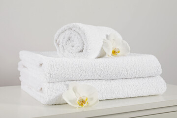 Obraz na płótnie Canvas Clean soft white towels with flowers on table against light grey background