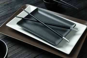 Stylish sushi dishware and chopsticks on black wooden table, closeup