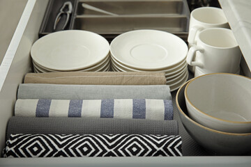 Open drawer of kitchen cabinet with different dishware and towels, closeup