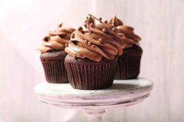 Delicious chocolate cupcakes with cream and beads on white stand, closeup