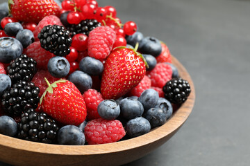 Mix of different fresh berries in bowl on grey table, closeup