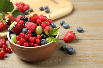 Mix of different fresh berries in bowl on wooden table. Space for text