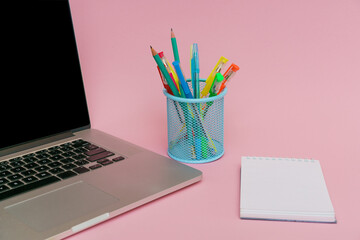 Laptop pens and colored pencils in blue stand and white stickers on pink background, back to school and business education concept