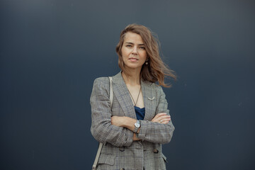Portrait of elegant young businesswoman standing with crossed arms in stylish blazer and squinting...