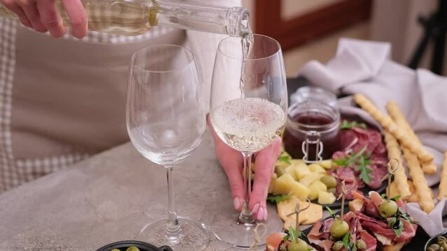 woman pouring wine to a glass from a bottle at domestic kitchen with meat and cheese plater on the table